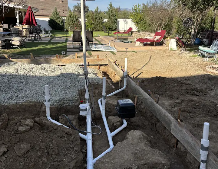 New PVC sewer and drain lines laid in an open trench with a cleanout, in a backyard ready for backfill