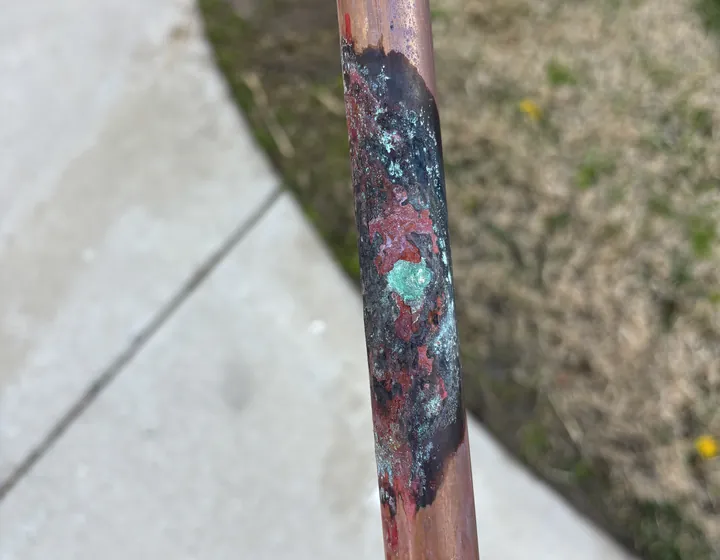 Close-up of a corroded copper water line with a pinhole leak, the kind of failure behind most emergency calls
