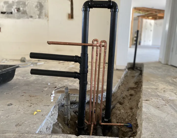 Slab leak repair in progress: new copper and ABS lines rising from a cut section of concrete floor