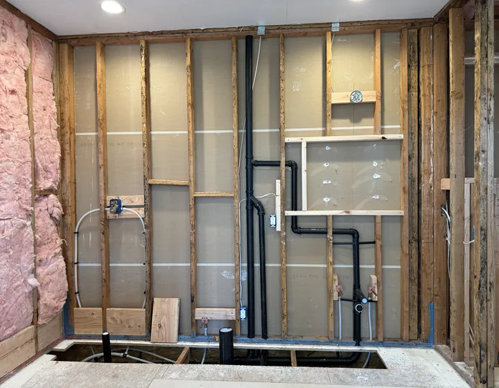 Bathroom wall opened to the studs during a repipe, with new supply and drain lines run before drywall