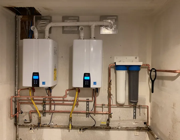 Two wall-mounted Navien tankless water heaters installed side by side with a sediment filter and new copper and gas lines