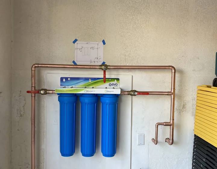 Three-stage whole-house water filtration system plumbed in copper with a bypass loop on a garage wall